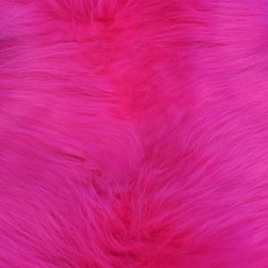 May include: A close-up shot of a bright pink faux fur fabric. The material has long, soft fibres, creating a textured surface. The background is a solid blue, providing contrast to the bright pink. This fabric is suitable for various craft projects.