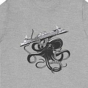 May include: A gray t-shirt featuring a black and white graphic of an octopus holding a cruise ship. The octopus has multiple tentacles and is centered on the shirt. The cruise ship is detailed with windows and railings.