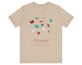 Könnte beinhalten: Beiges T-Shirt mit einer Grafik von bunten, schwebenden Büchern. Das Wort "Bibliophile" ist rot gedruckt, darunter die Definition "(n.) eine Person, die Bücher liebt". Ein tolles Geschenk für Leseratten.