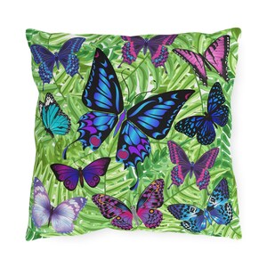 May include: Square throw pillow featuring a vibrant pattern of colorful butterflies in shades of blue, purple, pink, and teal. The butterflies are set against a background of green and white tropical leaves. The pillow has a soft, inviting appearance.