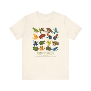 May include: A light beige t-shirt with a graphic of colorful frogs and the text "Batrachophile (n.) a person who loves frogs or toads".
