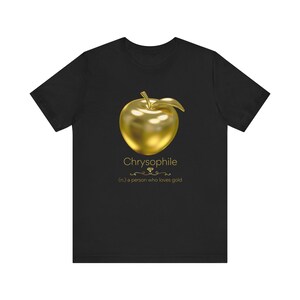 May include: Black t-shirt featuring a gold apple graphic. The text "Chryophile" is above the definition "(n.) a person who loves gold". The apple has a shiny, metallic appearance.