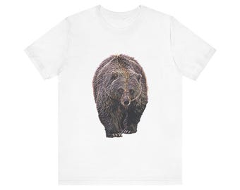 May include: White t-shirt featuring a detailed illustration of a brown bear. The bear is depicted in a realistic style, with fur and facial features. The design is centered on the shirt.