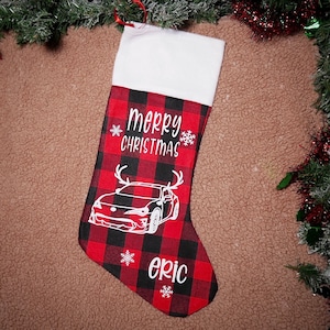 May include: Red and black plaid Christmas stocking with a white car and antlers, the text "merry christmas" and the name "eric" in white.