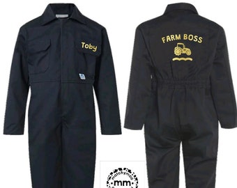 Puede incluir: Un mono de color azul marino oscuro con cuello, mangas largas y cierre frontal de botones. El bolsillo izquierdo del pecho tiene bordado el nombre Toby en amarillo. La espalda muestra el texto amarillo FARM BOSS sobre un icono de tractor.
