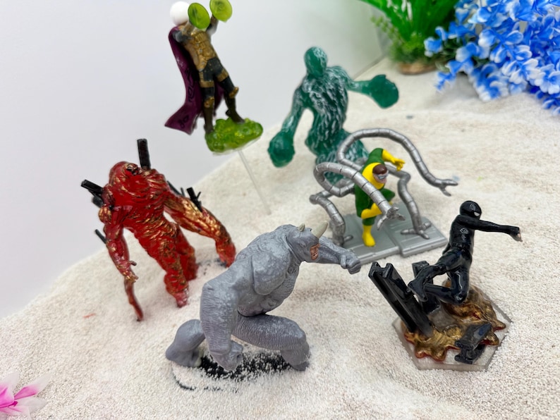 May include: A collection of colorful action figures featuring various characters. The figures include a red monster, a gray rhino-like figure, a green figure, a figure with metal arms, a black figure, and a figure with a purple cape.