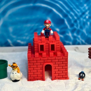May include: A red brick castle with a small figure of Mario standing on top. There is a green pipe, a white cloud with a figure of a yellow character, and a black and brown figure of a character from the Super Mario Bros. video game.