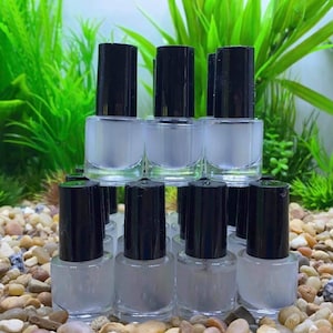 May include: A group of clear glass bottles with black caps, filled with a white liquid. The bottles are arranged in a pyramid shape on a bed of small, light brown stones.