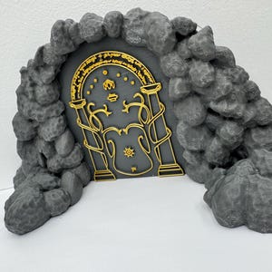 May include: A gray, stone-like archway with a gold-colored door. The door features intricate designs and text. The archway is made of textured, rounded stones. A decorative item for fans of fantasy literature.