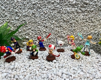 May include: A collection of 10 small plastic figurines of characters from the Super Mario video game franchise. The characters are posed in various athletic positions, including playing tennis, baseball, and skateboarding. The figurines are all brightly colored and have a cartoonish style.