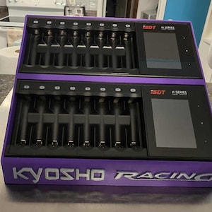 May include: A purple and black ISDT N Series battery charger with the Kyosho Racing logo. The charger has two sections with multiple charging slots and digital displays. The device is designed for charging batteries.