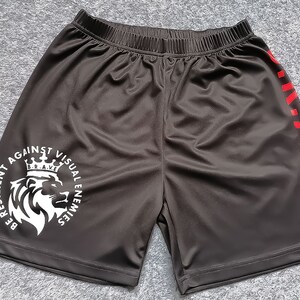 Op de afbeelding: Zwarte sport shorts met een witte leeuw afbeelding en de tekst "Be Resilient Against Visual Enemies" en een rode "B.R.A.V.E." aan de zijkant.
