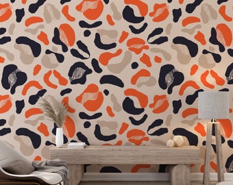 May include: A living room interior with a wall covered in a wallpaper featuring an abstract pattern of orange, beige, and black shapes. A brown wooden bench sits in front of the wall, with a white armchair and a floor lamp to the right.