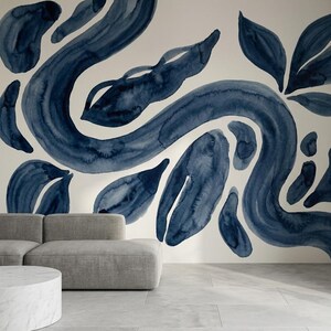 Può includere: Un interno moderno con un murale con forme astratte blu ad acquerello. Il design del murale include linee fluide e forme simili a foglie su uno sfondo color crema. Un divano grigio e un tavolino in marmo sono in primo piano.