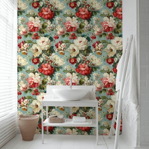 May include: A bathroom with a floral wallpaper featuring large red and white roses on a light blue background. The room has a white sink, a white shelf, and a white wooden floor. A woven basket and a white towel are also visible.