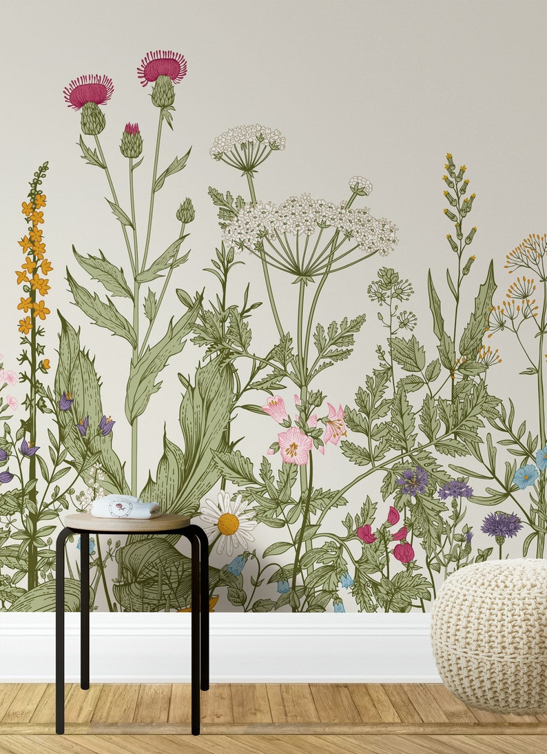 May include: A white wall with a floral wallpaper featuring a variety of green leaves, pink, white, and purple flowers. A small black metal stool with a wooden top sits in front of the wall. A white knitted footstool sits on the floor.