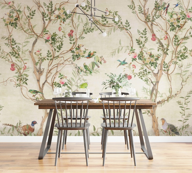 May include: A dining room scene featuring a wooden table and chairs set against a floral wallpaper backdrop. The wallpaper showcases a botanical design with trees, birds, and flowers in shades of green, pink, and beige. The table is set with glassware.