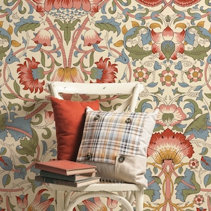 Puede incluir: Una silla de mimbre blanca con dos almohadas, una roja y otra a cuadros, y tres libros apilados en el asiento. La silla est&aacute; delante de una pared cubierta con un papel tapiz floral con un patr&oacute;n repetitivo de flores rojas, rosas, amarillas y azules.