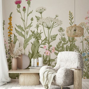 May include: A living room interior design featuring a white fluffy armchair with a throw blanket, a wooden coffee table, and a beige wall with a floral wallpaper design. The wallpaper features a variety of flowers and plants in shades of pink, green, and yellow.