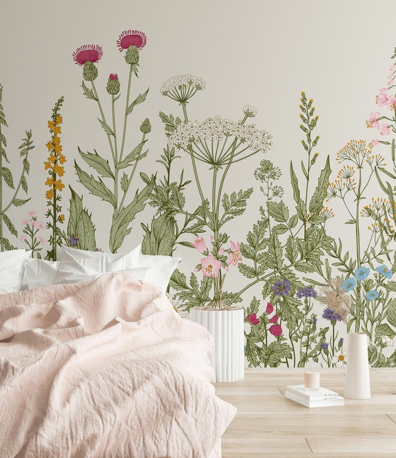 May include: A bedroom with a floral wallpaper featuring a variety of flowers and plants in shades of green, pink, yellow, and blue. A white bed with a pink blanket is in the foreground. A white vase with a flower arrangement is on the right side of the image.
