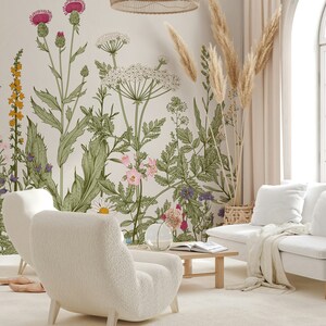 May include: A living room interior with two white fluffy armchairs, a white couch, a wooden coffee table, and a floral wallpaper with a light beige background. The wallpaper features a variety of flowers and plants, including thistles, daisies, and ferns. There are also dried pampas grass stalks in a woven basket.