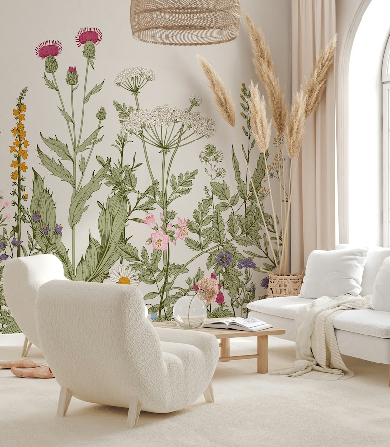May include: A living room interior with two white fluffy armchairs, a white couch, a wooden coffee table, and a floral wallpaper with a light beige background. The wallpaper features a variety of flowers and plants, including thistles, daisies, and ferns. There are also dried pampas grass stalks in a woven basket.
