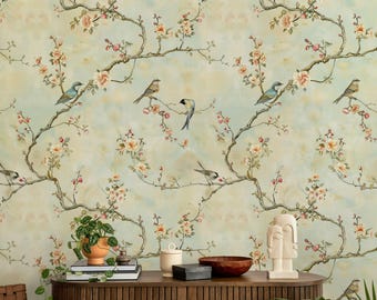 May include: Wallpaper featuring a repeating pattern of brown tree branches with pink flowers and small birds in shades of blue, grey, and brown against a pale, mottled light green background. The design creates a continuous botanical scene.