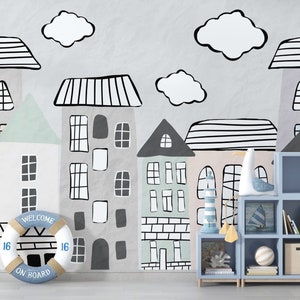 May include: A light blue bookshelf with six shelves, filled with books and decorative items. The bookshelf is in front of a wall with a whimsical mural of houses and clouds, featuring a life preserver with the text "Welcome on Board".