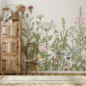 May include: A vintage-style wooden cabinet with two doors and three shelves sits next to a chair in front of a wall with a floral wallpaper featuring a variety of flowers and plants in shades of pink, green, blue, and yellow.