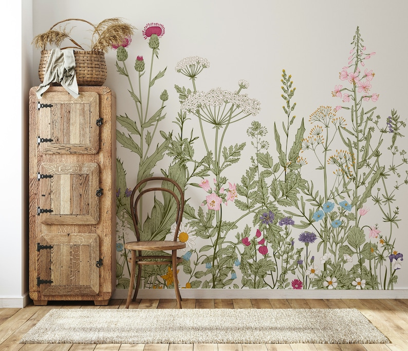 May include: A vintage-style wooden cabinet with two doors and three shelves sits next to a chair in front of a wall with a floral wallpaper featuring a variety of flowers and plants in shades of pink, green, blue, and yellow.