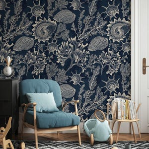 Puede incluir: Un papel pintado de color azul marino oscuro con un patrón repetitivo de ilustraciones de líneas color crema de varias conchas, corales y plantas marinas. El intrincado diseño náutico cubre la pared detrás de un sillón azul verdoso.