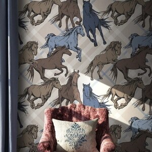 May include: A beige wallpaper with a repeating pattern of brown and blue horses running in different directions. The wallpaper is in a room with a pink armchair and a blue rug.