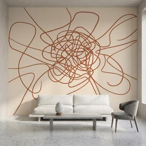 May include: A modern living room with a beige wall featuring a large, abstract brown line drawing. A white sofa, a gray chair, and a concrete coffee table with a decorative stone object complete the minimalist decor. The floor is marble.