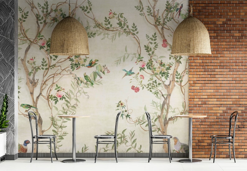 May include: A cafe interior featuring a floral mural with birds, tables, and chairs. Two woven pendant lights hang above the tables. The wall on the right is brick, and the floor is white.