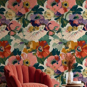 May include: A vibrant floral wallpaper featuring large, colorful blooms in shades of red, pink, purple, and yellow against a cream background. A coral-colored armchair and a small side table with a vase of dried flowers are in the foreground.