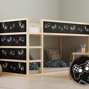 Op de afbeelding: Een houten stapelbed met een zwart schoolbord hoofdeinde met een herhalend patroon van witte videogame controllers en spelcartridges. Het bed is opgemaakt met een zwart-wit gepatroneerd dekbed en een zwart-wit gepatroneerd kussen. Een zwart-witte videogame controller is te zien op een zwart-witte achtergrond in de rechterbenedenhoek van de afbeelding.
