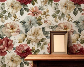 May include: A rectangular wooden table with a light brown finish stands against a wall covered in floral wallpaper featuring large cream, dusty pink, and deep red blossoms with green leaves. A blank picture frame and a glass bowl sit on top.