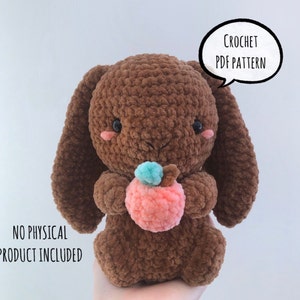 May include: Crochet pattern for a brown plush bunny holding a pink apple. The pattern is available as a PDF download. "CROCHET PDF PATTERN" is written in a speech bubble above the bunny. "NO PHYSICAL PRODUCT INCLUDED" is written below the bunny.