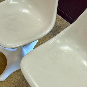 Pode incluir: Tr&ecirc;s cadeiras de pl&aacute;stico branco com base em forma de estrela. As cadeiras est&atilde;o dispostas em fila sobre um tapete bege.