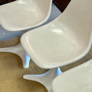 Pode incluir: Tr&ecirc;s cadeiras brancas de fibra de vidro com uma base &uacute;nica em forma de estrela. As cadeiras est&atilde;o dispostas em fila, com a base de cada cadeira vis&iacute;vel.