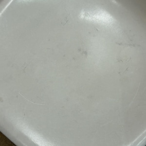 Pode incluir: Close-up de um assento de cadeira de pl&aacute;stico branco com arranh&otilde;es e marcas vis&iacute;veis.