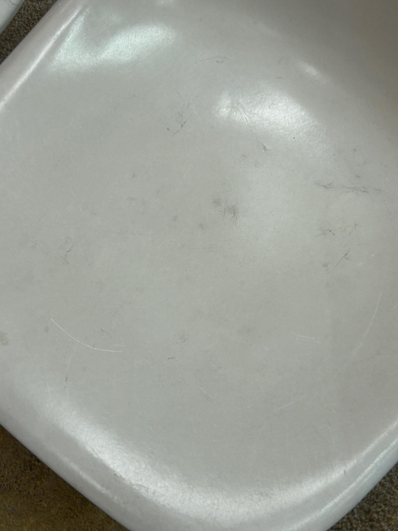 Pode incluir: Close-up de um assento de cadeira de pl&aacute;stico branco com arranh&otilde;es e marcas vis&iacute;veis.