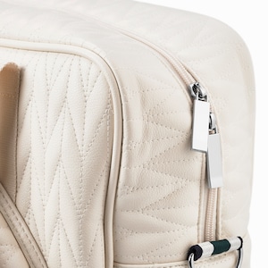 Close up photo of a tennis bag in quilted white vegan leather with wimbledon green webbing and solid silver metal pullers.