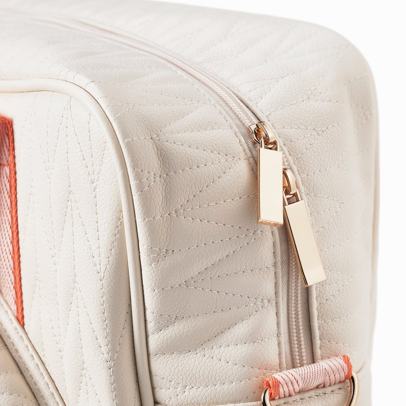 Close up photo of a tennis bag in quilted white vegan leather with orange webbing and solid golden metal pullers.
