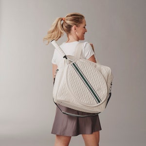 Woman holding a tennis bag in quilted white vegan leather with wimbledon green webbing and solid silver metal pullers.