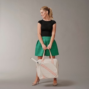 Woman holding a tennis bag in quilted white vegan leather with orange webbing and solid golden metal pullers.