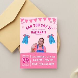 May include: A pink birthday invitation with the text "Can You Say 2!" and "Mariana's Birthday!" features illustrations of overalls. The invitation includes the date, time, and RSVP information. An envelope is in the background.