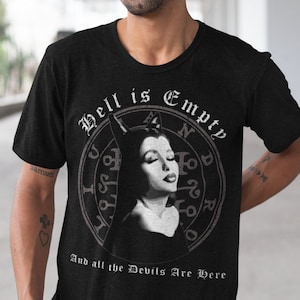 Puede incluir: Camiseta negra con el texto "Hell is Empty" sobre un gráfico circular de una mujer con cuernos de diablo. El texto "And all the Devils Are Here" está debajo del gráfico. La camiseta la lleva una persona.