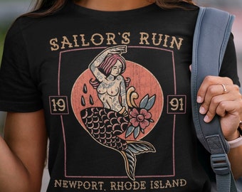 Op de afbeelding: Zwart T-shirt met een vintage-stijl afbeelding van een zeemeermin met de tekst "Sailor's Ruin 1991 Newport, Rhode Island".