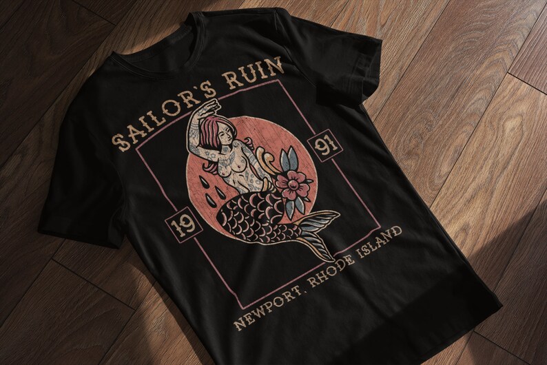 May include: Black t-shirt with a vintage-style graphic of a mermaid with a flower and the text "Sailor's Ruin 19 91 Newport, Rhode Island".